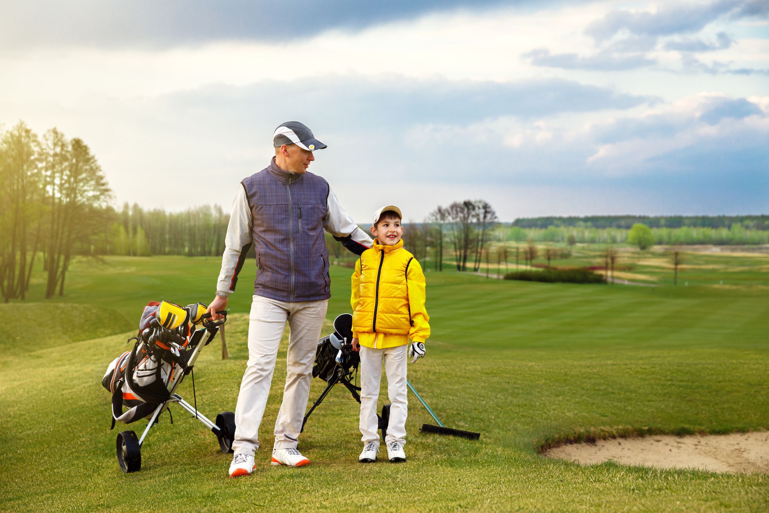 A father and his son walking with their golf club bags to the next hole on a beautiful golf course
